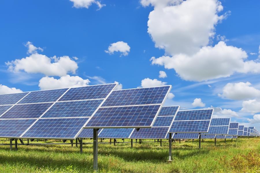 Solar farm on green grass with a bright blue cloud covered sky. 